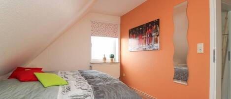 A bedroom with a sloped ceiling, a bed with a quilt, pillows, a window with a view, and a wall-mounted mirror.