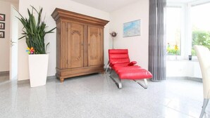 Quarto com um armário de madeira, uma cadeira vermelha, um vaso de planta e uma janela com cortinas.