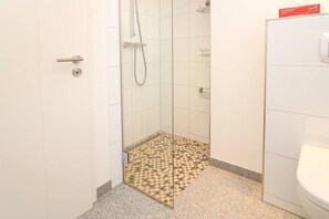 A bathroom with a shower, a toilet, and a patterned floor mat. - Rote & Grüne Mühle (Krummhoern)