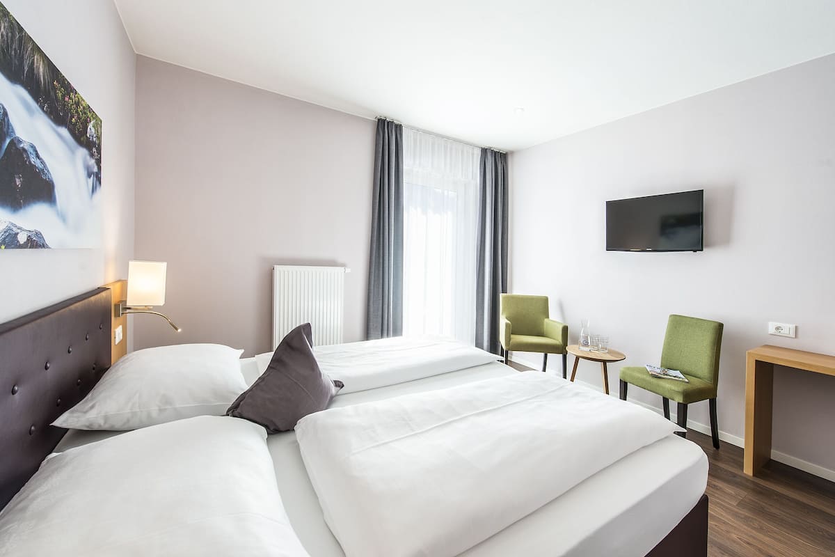 Ein Hotelzimmer mit zwei Betten, einem Fernseher, einem Schreibtisch und einem Stuhl.