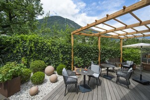 An outdoor patio with wooden pergola, seating, and potted plants.