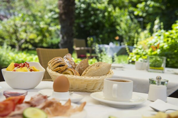 A breakfast setting with a wicker basket of bread, a bowl of fruit, and a cup of coffee on a table. - Hotel Jardis (Lana)