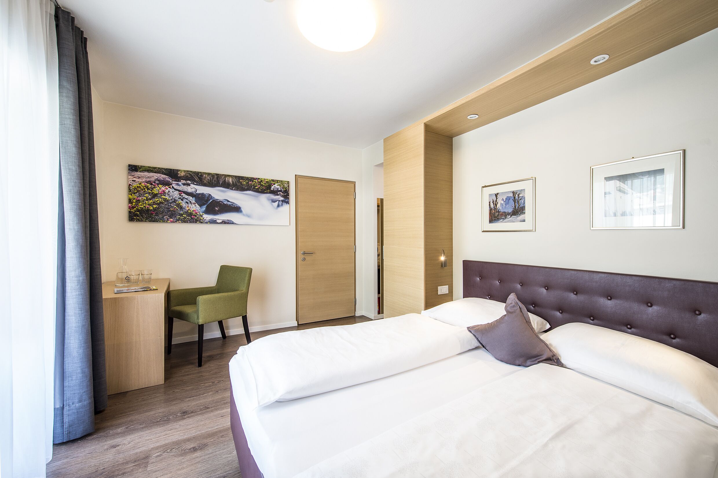 A hotel room with a bed, a desk, a chair, and a painting on the wall.