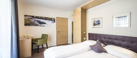 A hotel room with a bed, a desk, a chair, and a painting on the wall.