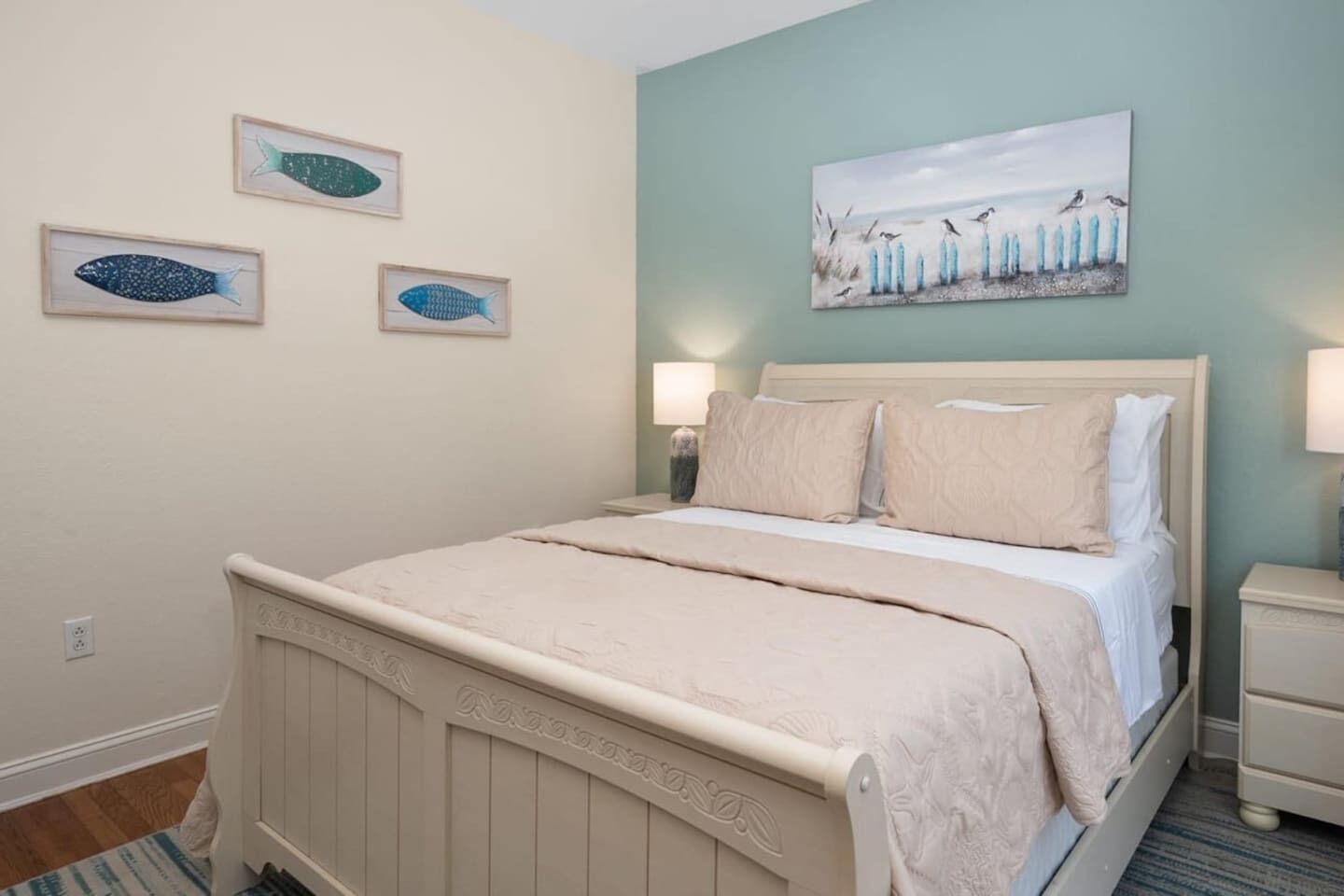 A bedroom with a bed, a nightstand, and wall art including fish and birds.