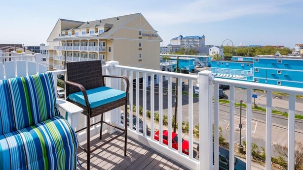 A balcony with a wicker chair and a striped sofa, overlooking a cityscape with buildings and a road. - Walk to BeachBoardwalk, GameRoom, Bikes, BeachGear (Ocean City)