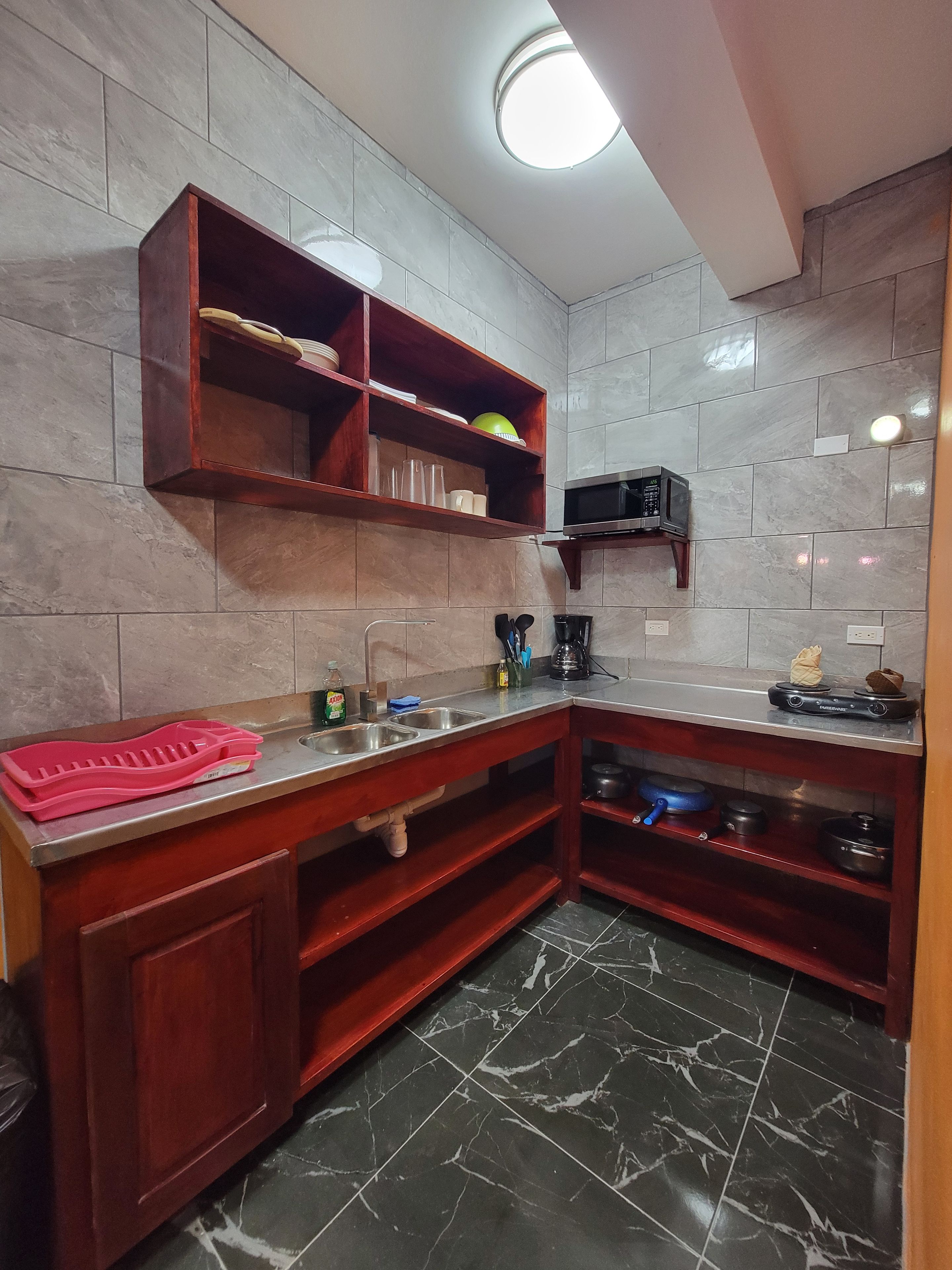 A kitchen with a marble floor, wooden cabinets, a built-in microwave, and a shelf with dishes.