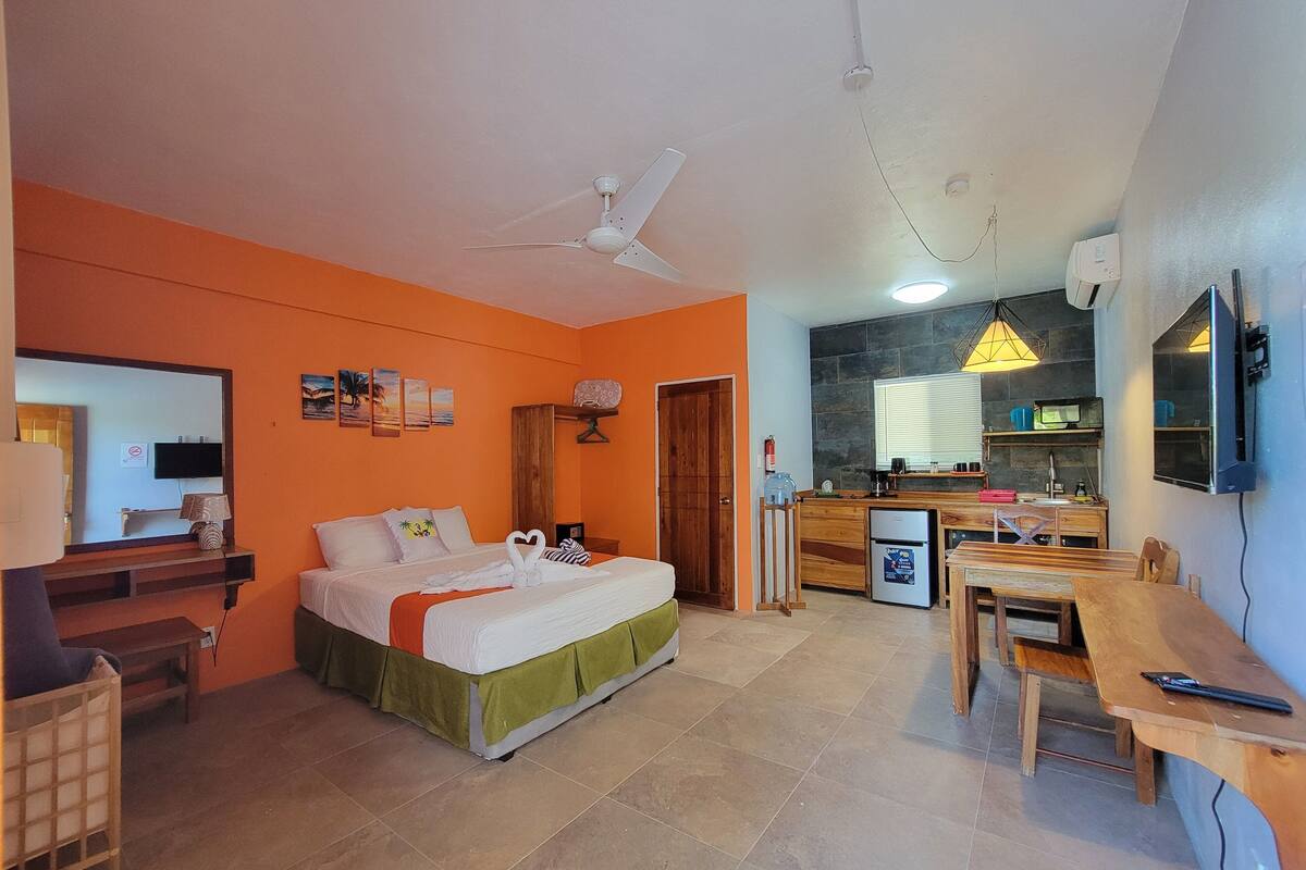 A compact hotel room with a bed, a small kitchenette, a dining area, and a bathroom.