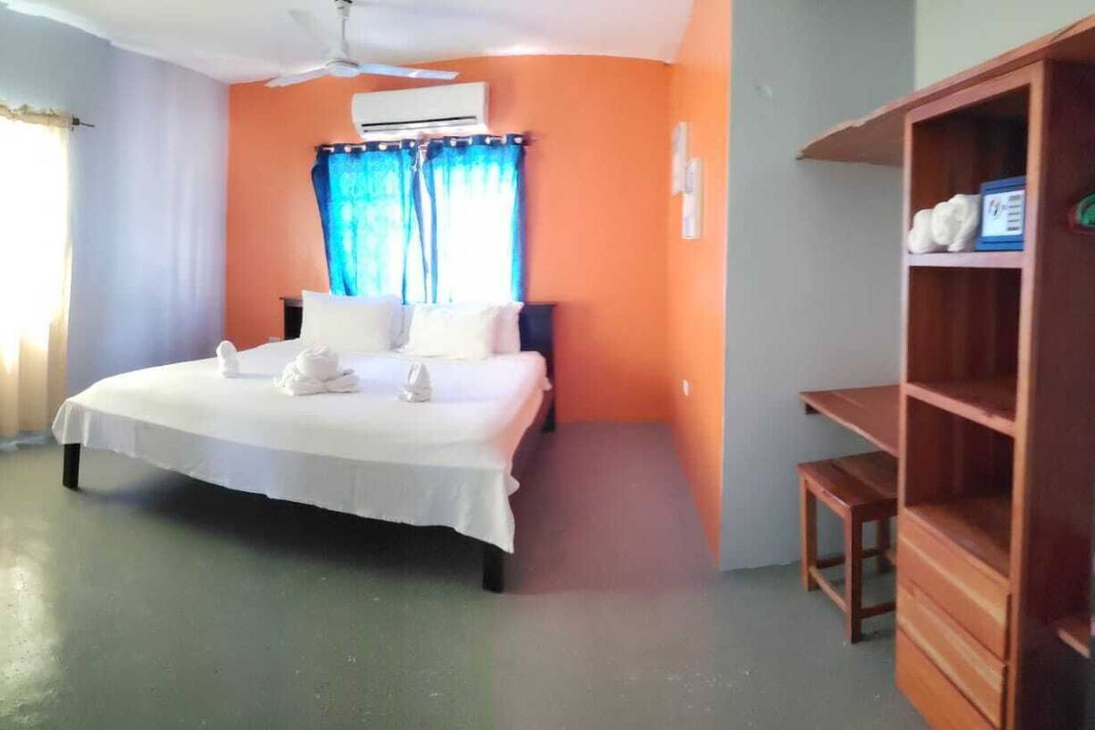 A bedroom with a bed, an air conditioner, a wooden shelf, and a desk.