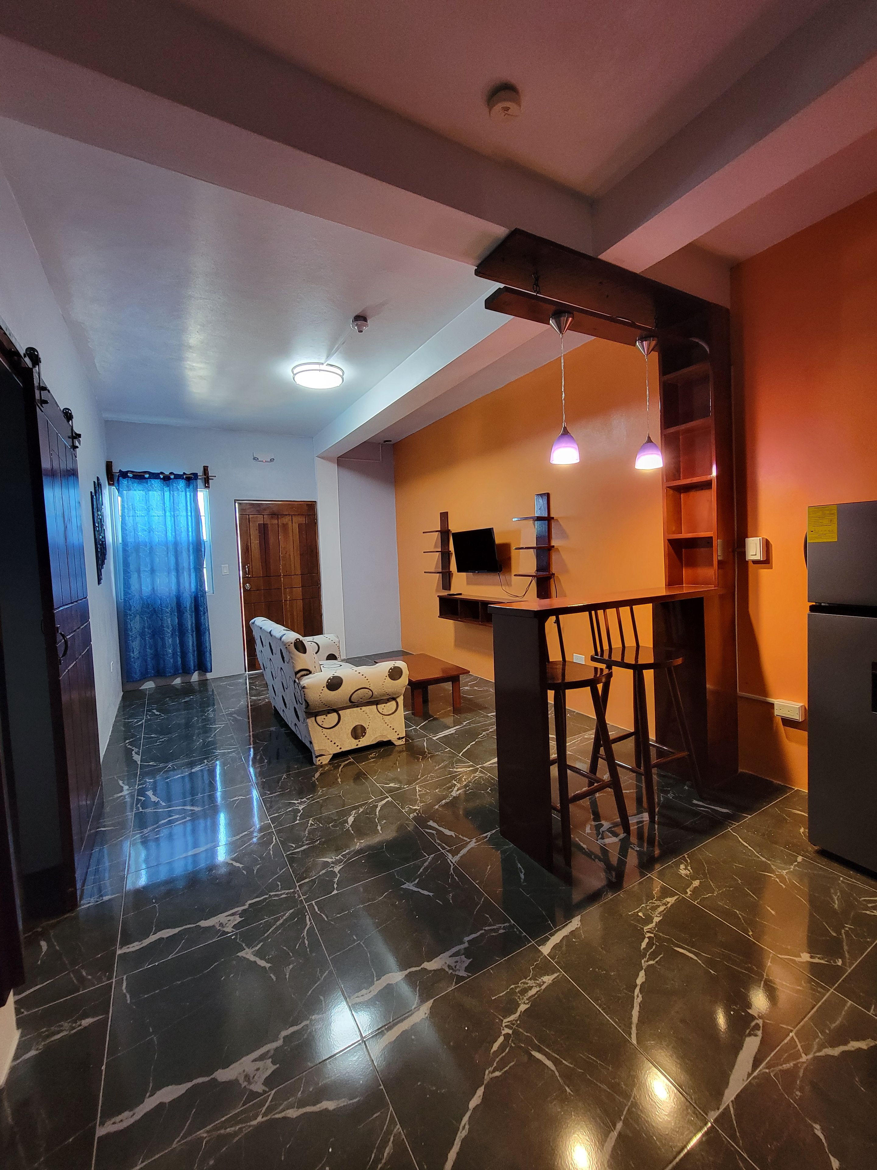 A modern kitchen with a marble floor, a dining area with bar stools, and a built-in TV.