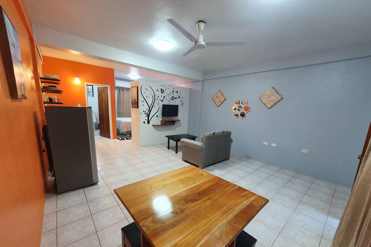 A spacious living area with a wooden dining table, a grey sofa, and a ceiling fan.