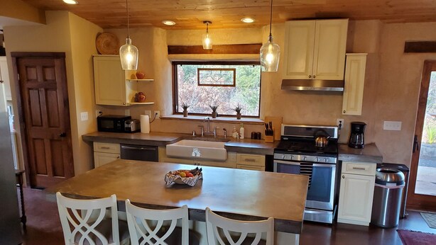 A kitchen with wooden cabinets, a central island with chairs, a sink, and a stove. - Hiking, mt biking, 44 acres to explore, 20 min outside of Santa Fe (Santa Fe)