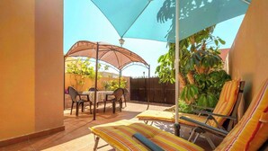 Un patio con una mesa y sillas, una silla reclinable a rayas y una sombrilla grande que da sombra.