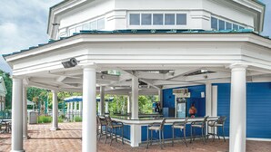 A covered outdoor seating area with white columns and blue accents, featuring a bar and chairs.