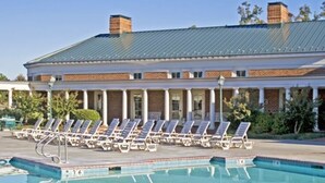 A swimming pool with lounge chairs, a covered patio, and a building with columns and a brick facade.