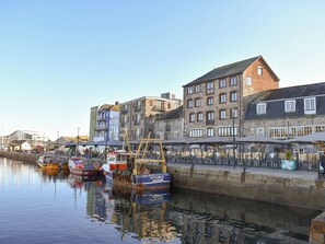 Margem com barcos atracados, edifícios de pedra e céu claro.