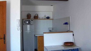 Uma cozinha compacta com micro-ondas, geladeira e uma mesa pequena com uma tigela.