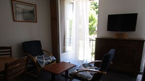 Uma sala de estar com uma mesa de madeira, duas poltronas de balanço, uma televisão em um móvel e uma janela com cortinas.