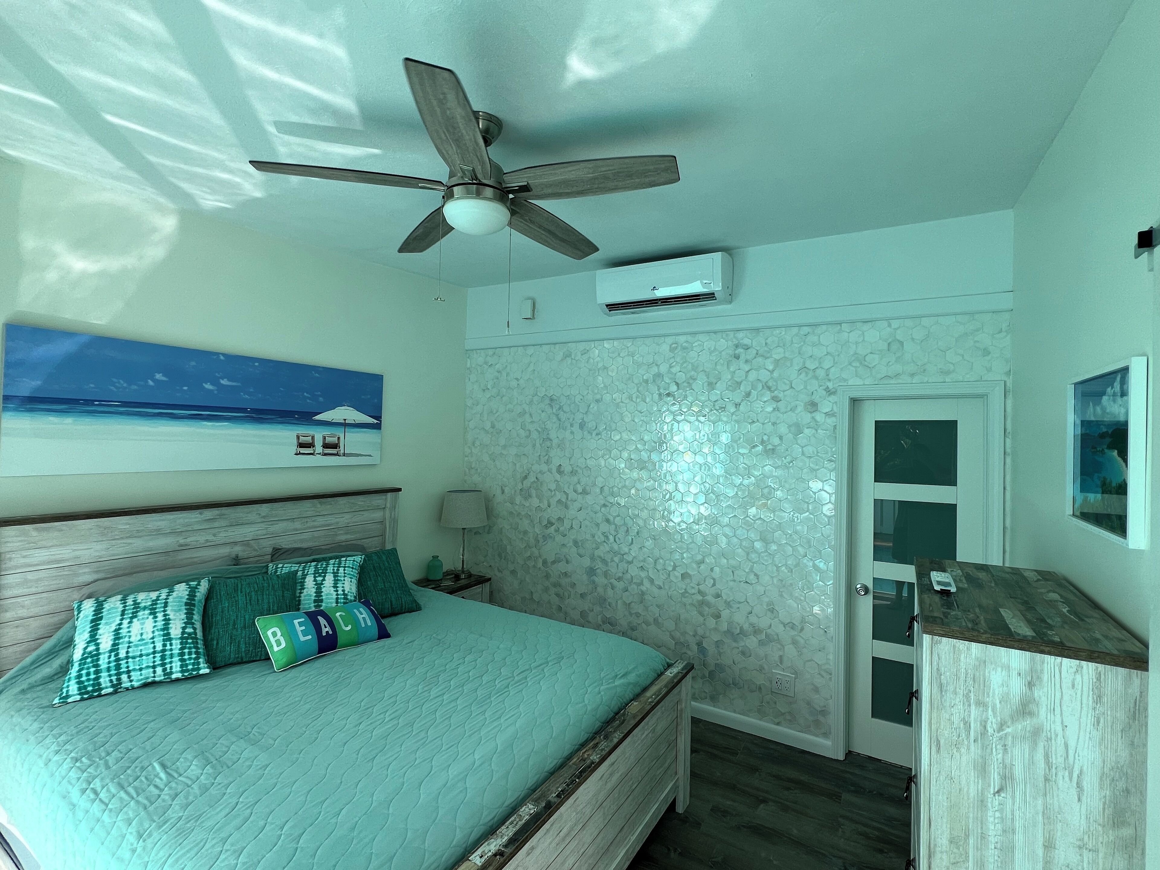 Ein Schlafzimmer mit einem Bett, einem Deckenventilator, einer Wandklimaanlage, einer Tür und einem Fenster.