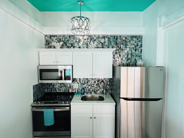 A kitchen with white cabinets, a stainless steel refrigerator, a microwave, and a stove.