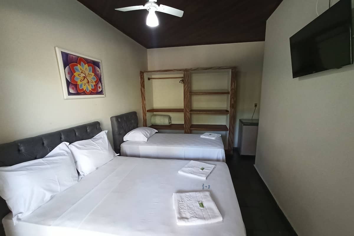 Ein Hotelzimmer mit zwei Betten, einem Deckenventilator, einem kleinen Fernseher und einem Bild an der Wand.