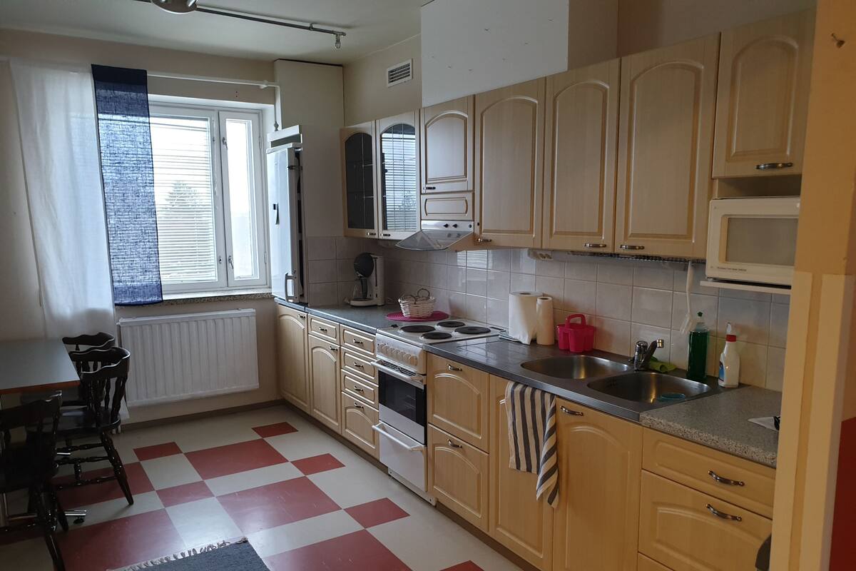 A kitchen with wooden cabinets, a stove, a sink, and a window with blinds.
