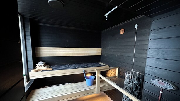A small, dark-themed room with a bunk bed, a small table, and a heater. - Kurimon majatalo (Suomussalmi)
