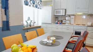 A dining area with a table set for two, a bowl of fruit, and a kitchen in the background. - Kurimon majatalo (Suomussalmi)