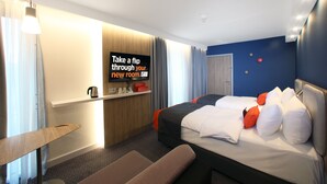 Une chambre d’hôtel moderne équipée d’un lit, d’un bureau, d’une chaise et d’un téléviseur fixé au mur.