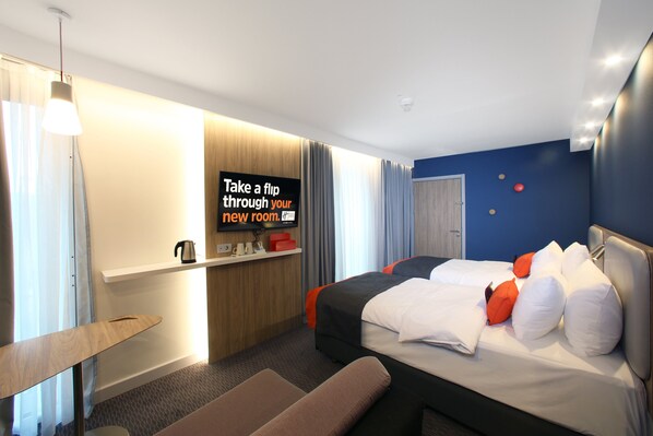 Una habitación de hotel moderna con cama, escritorio, silla y televisor montado en la pared.