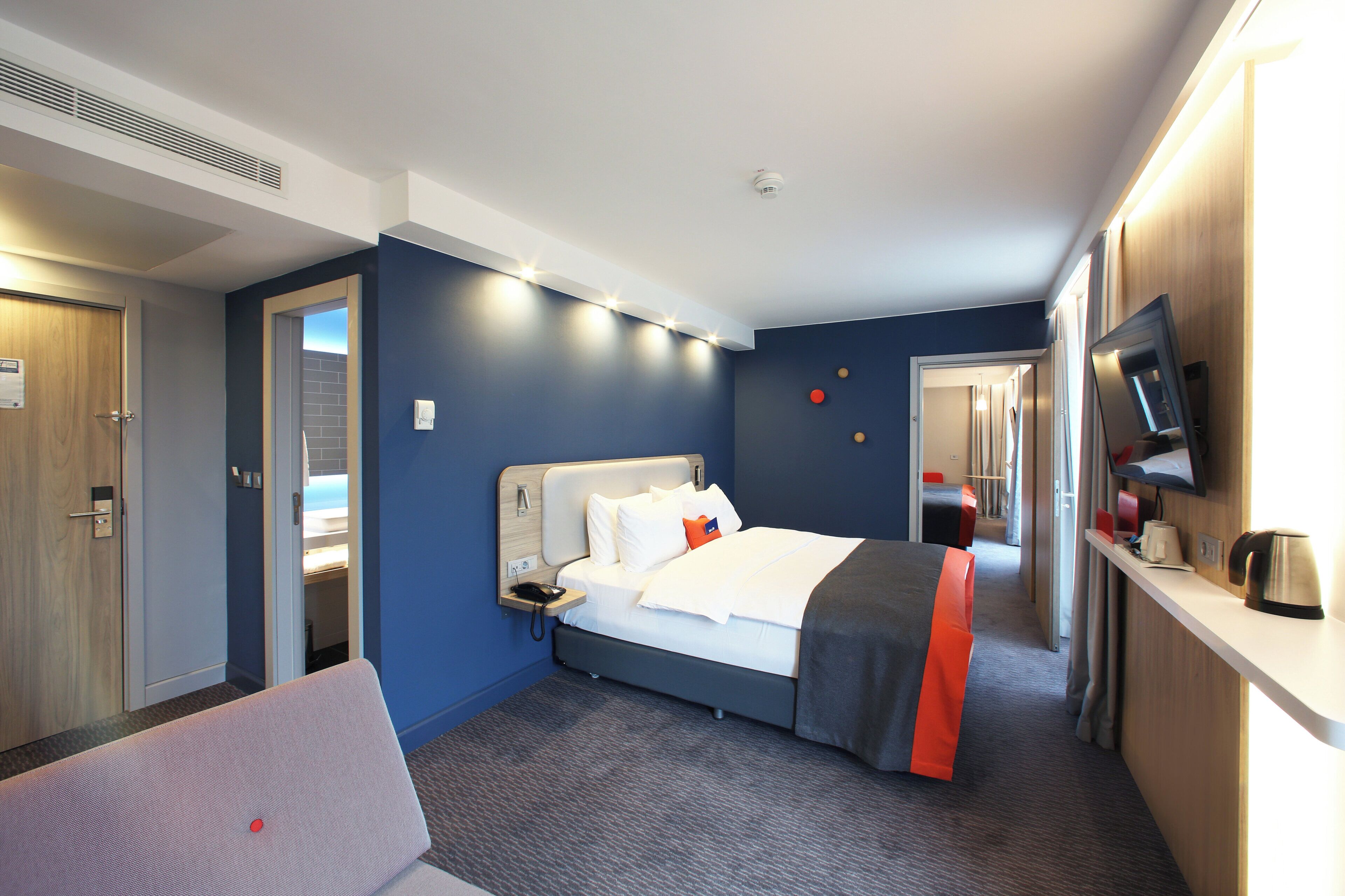 Habitación de hotel con cama, mesita de noche, televisor y vistas al pasillo.