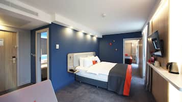 Habitación de hotel con cama, mesita de noche, televisor y vistas al pasillo.