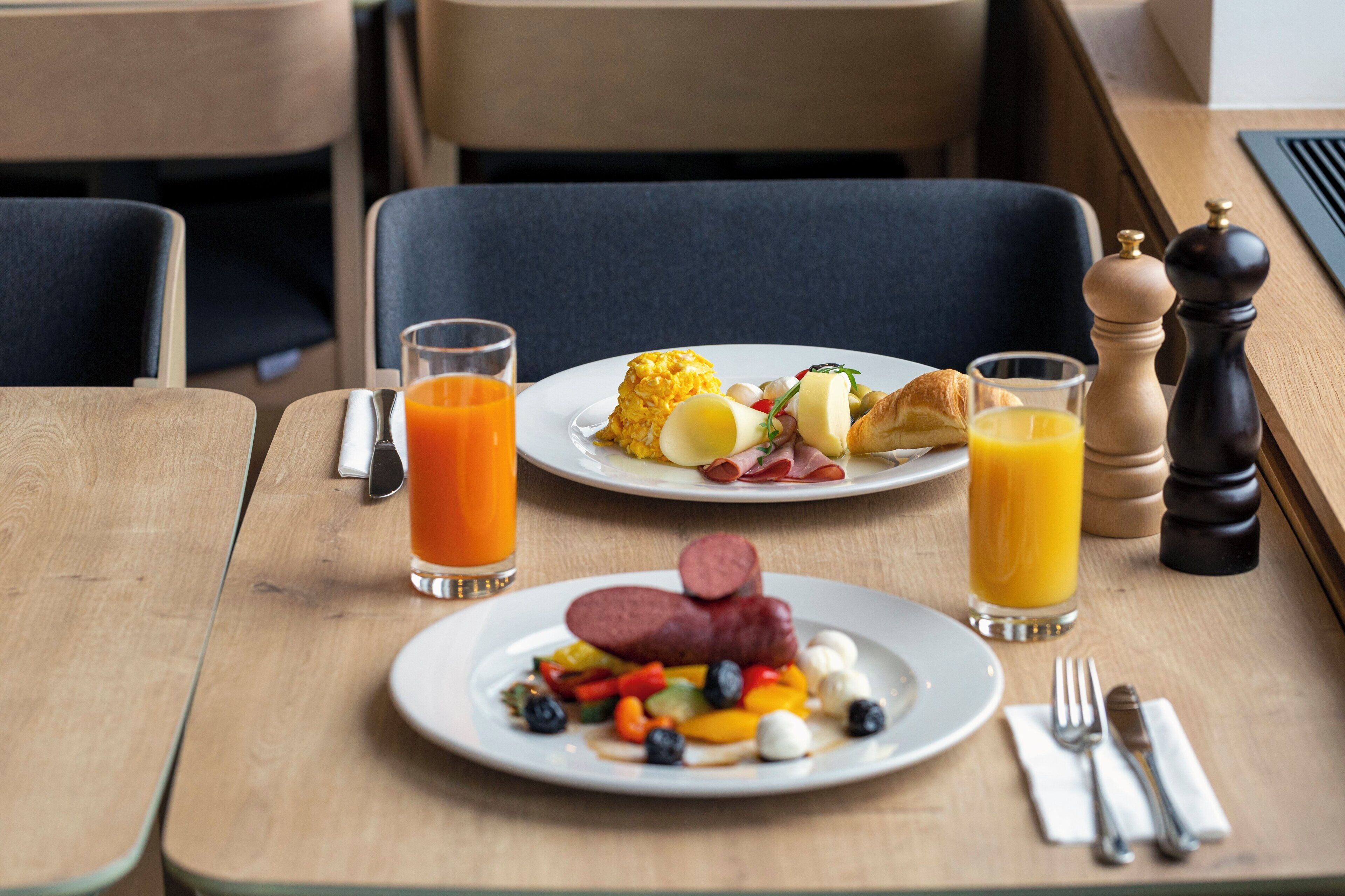 A breakfast setting with plates of food, glasses of orange juice, and a salt and pepper shaker on a wooden table.