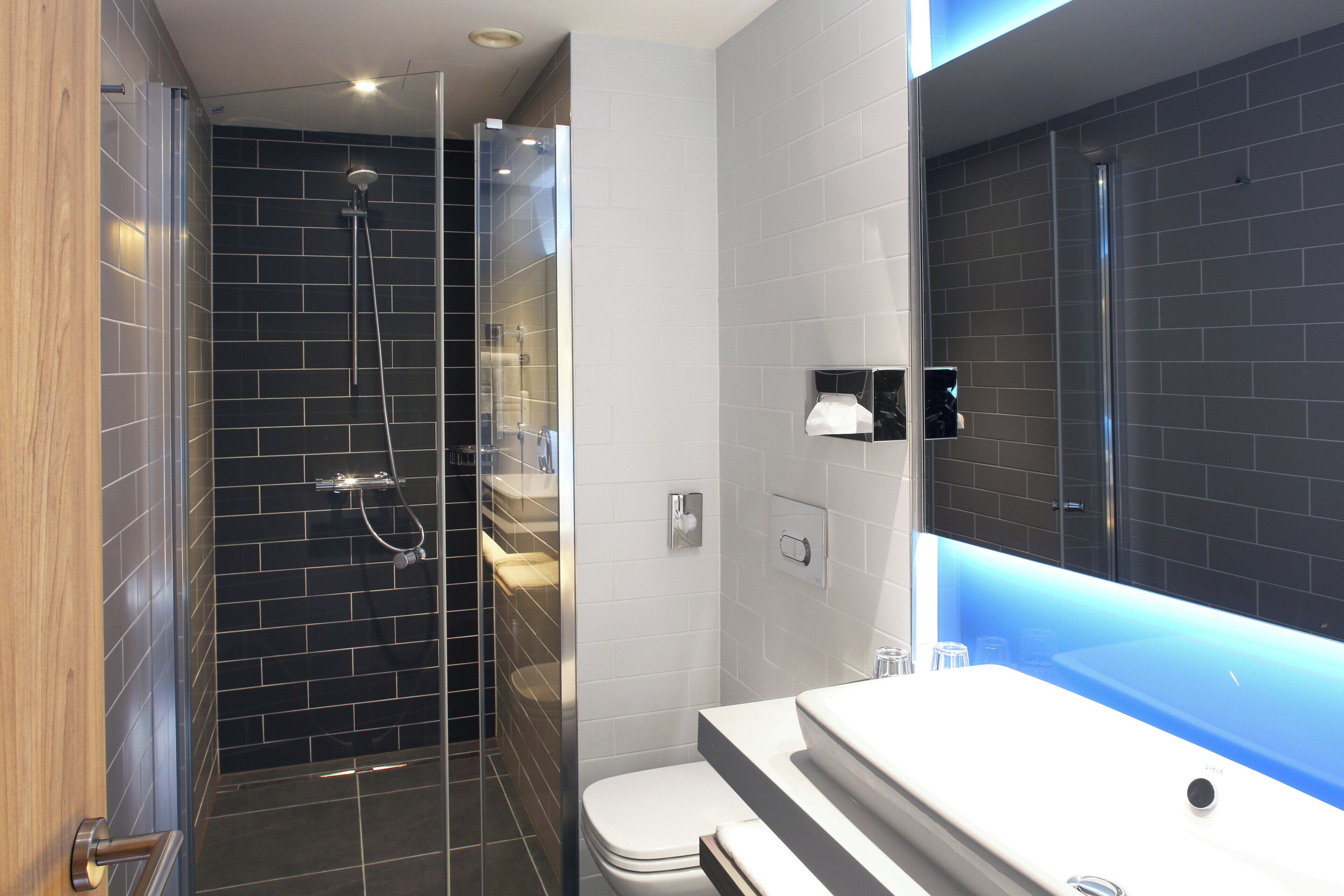 A modern bathroom with a glass-enclosed shower, a white sink, and a large mirror.