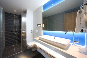 Un baño moderno con ducha envuelta en vidrio, un lavabo blanco y un mueble de tocador de madera.
