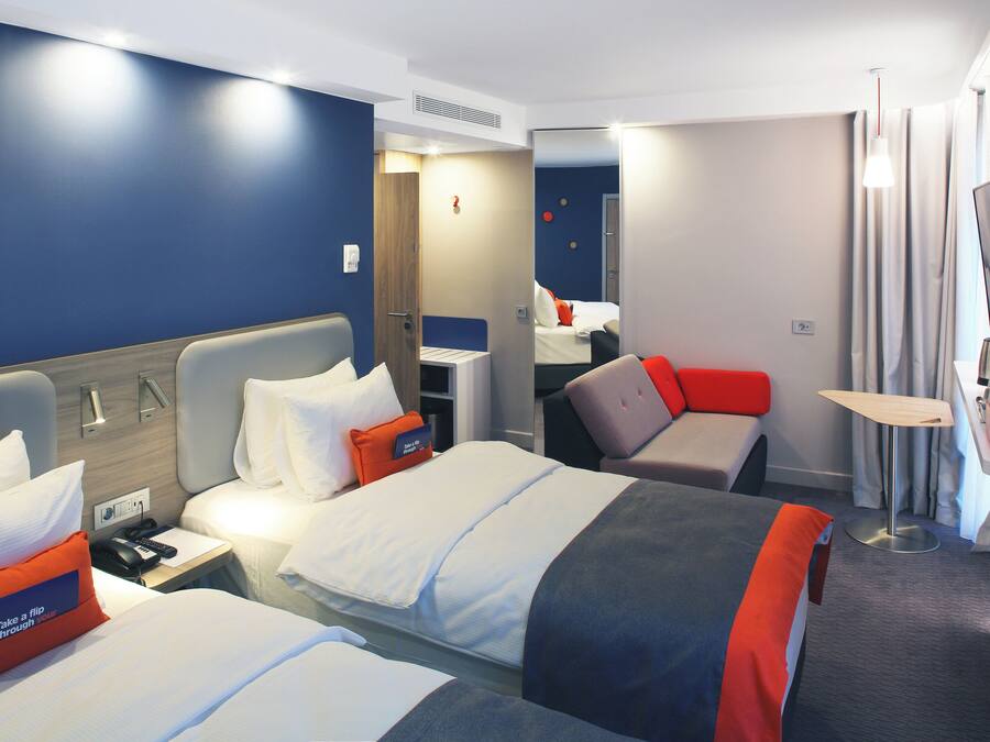 Habitació d'hotel amb dos llits, un escriptori, una cadira, un televisor i una taula petita.