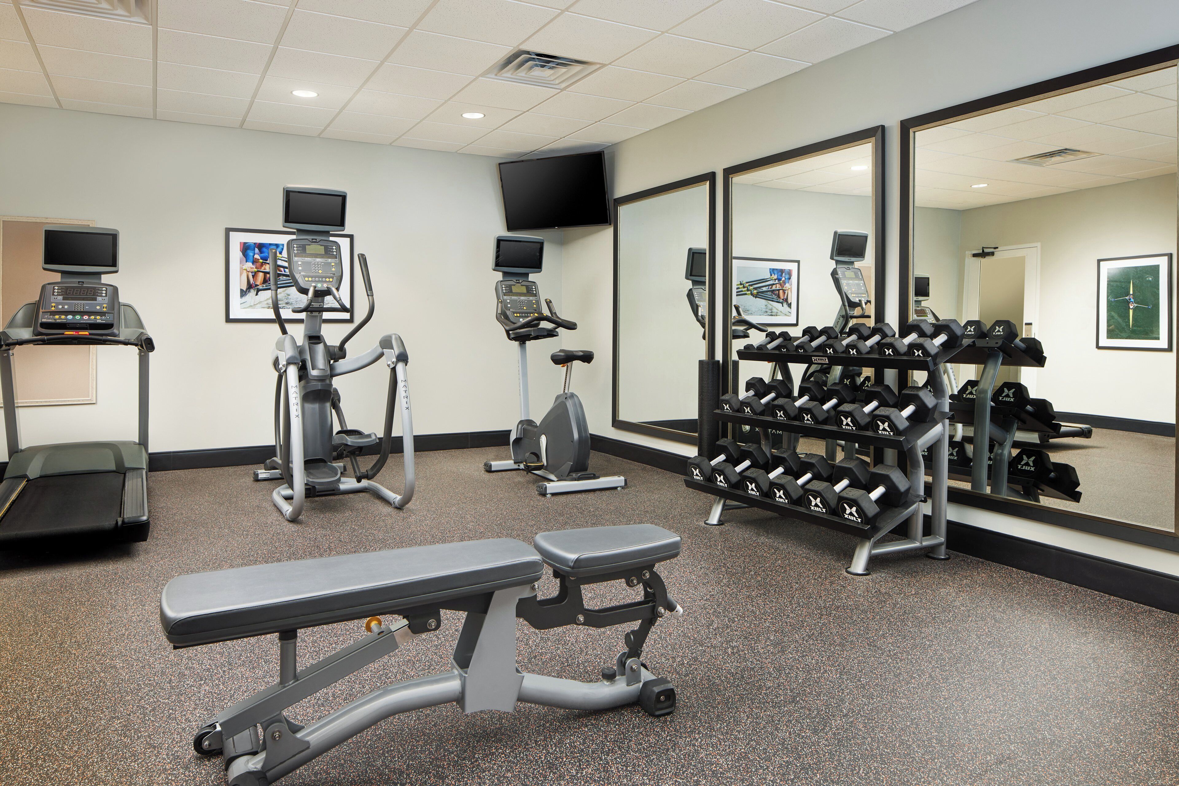 A gym with treadmills, an elliptical, a bench, and a rack of dumbbells.