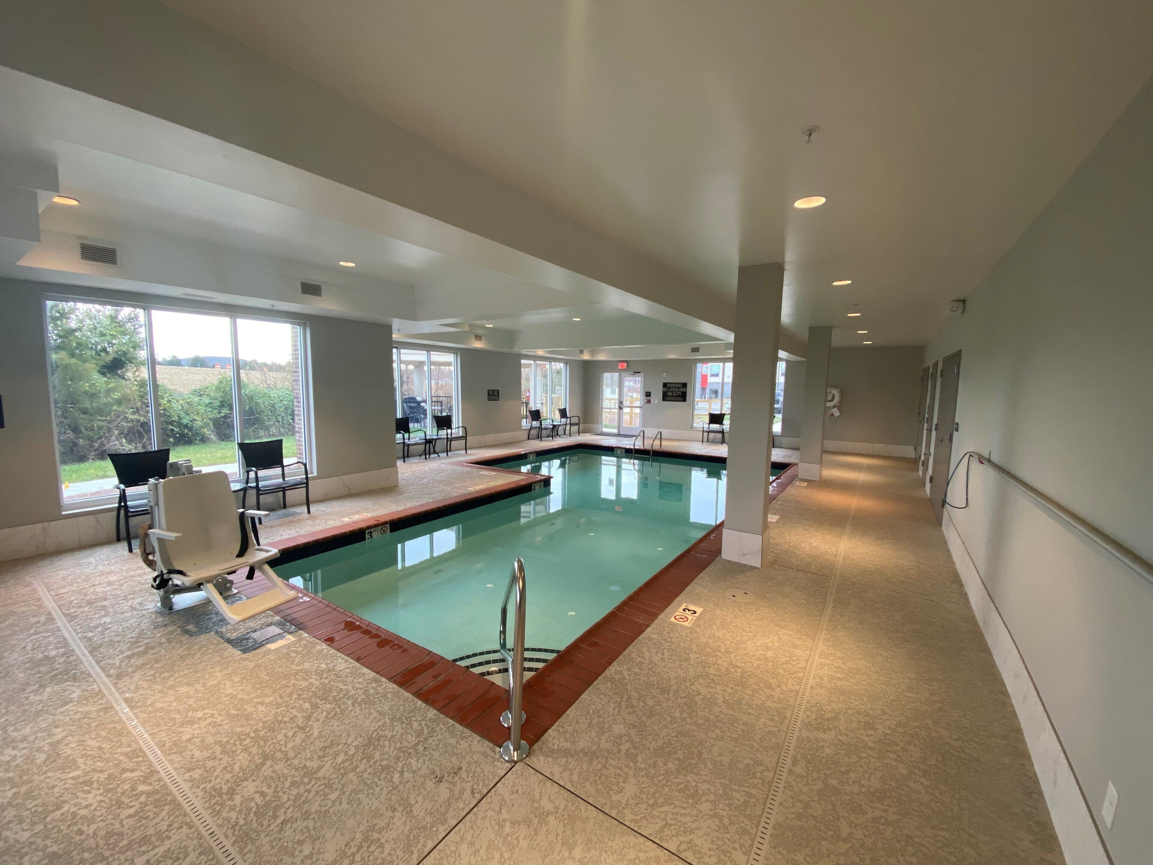 A swimming pool with a tiled deck, chairs, and a view of the outdoors.