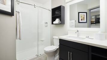 Une salle de bain moderne avec une douche à l’italienne en verre, des toilettes blanches, un meuble-lavabo noir avec un miroir et un tableau encadré au mur.