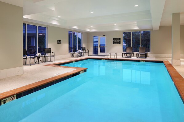 A large indoor swimming pool with clear blue water, surrounded by windows and chairs.