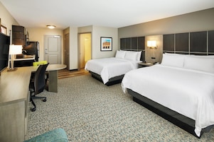 A hotel room with two beds, a desk with a chair, a small table, and a TV.
