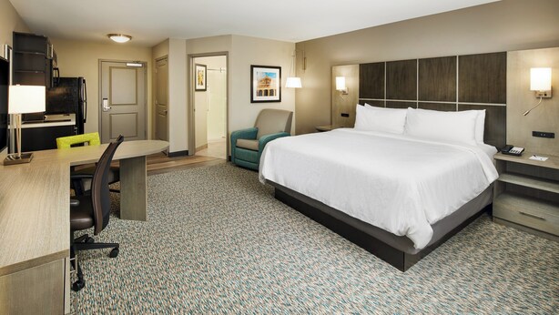 A hotel room with a large bed, a desk with a chair, a small armchair, a desk lamp, and a nightstand with a phone.