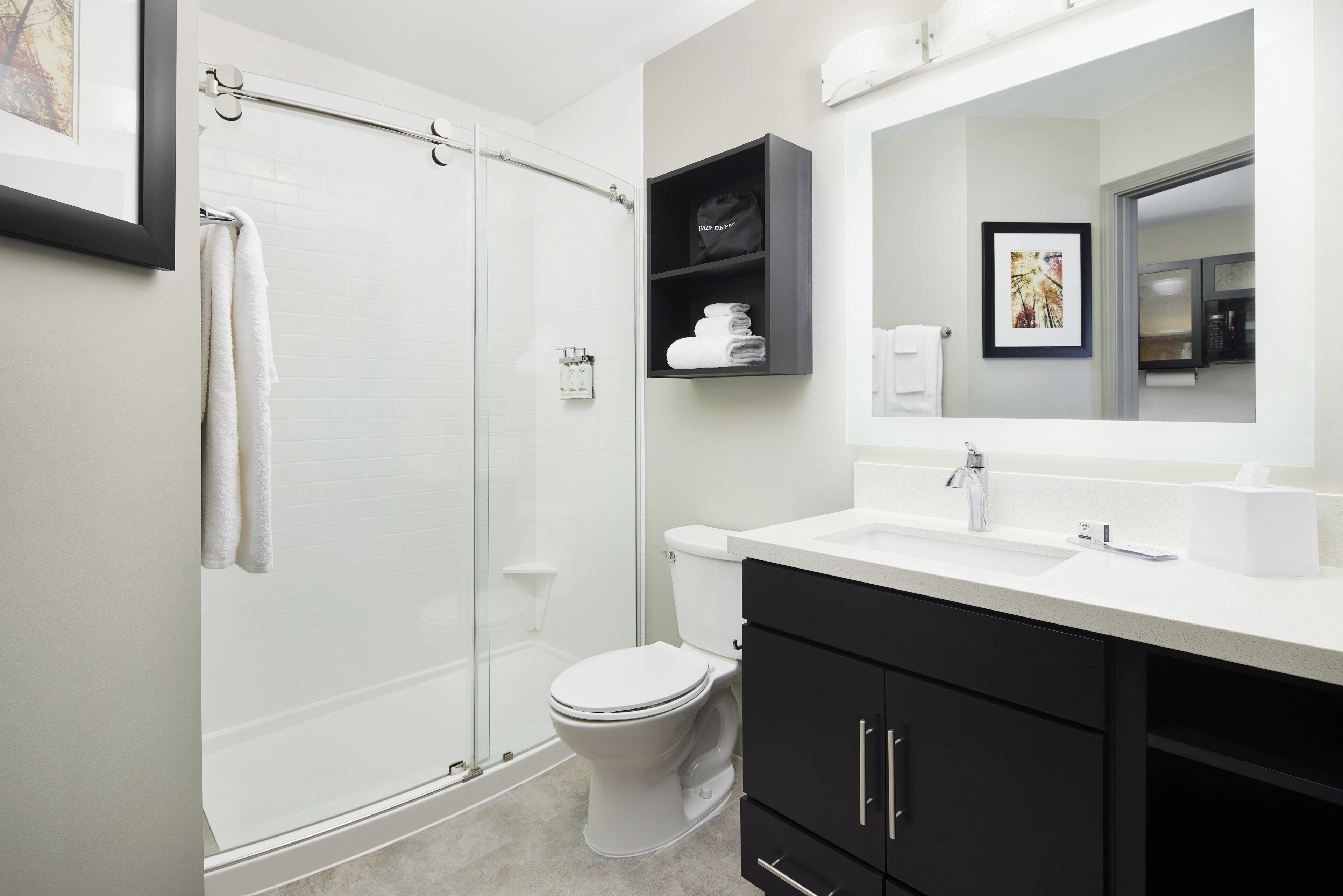 A modern bathroom with a glass shower enclosure, a white toilet, and a black vanity with a mirror above the sink.
