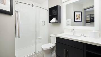 A modern bathroom with a glass shower enclosure, a white toilet, and a black vanity with a mirror above the sink.