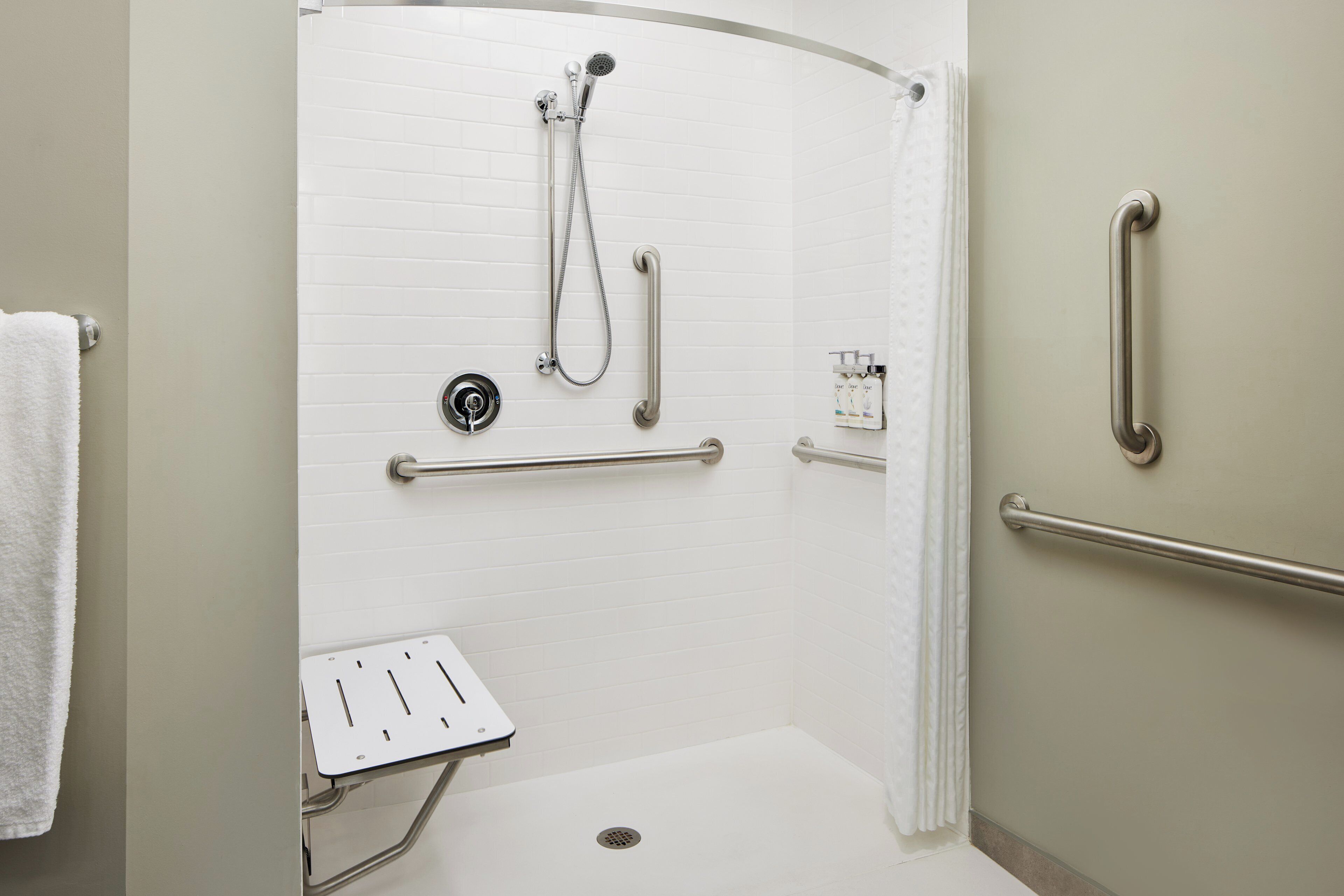 Ducha accesible para personas con discapacidad, con barras de apoyo, cabezal de ducha manual y panel de control.