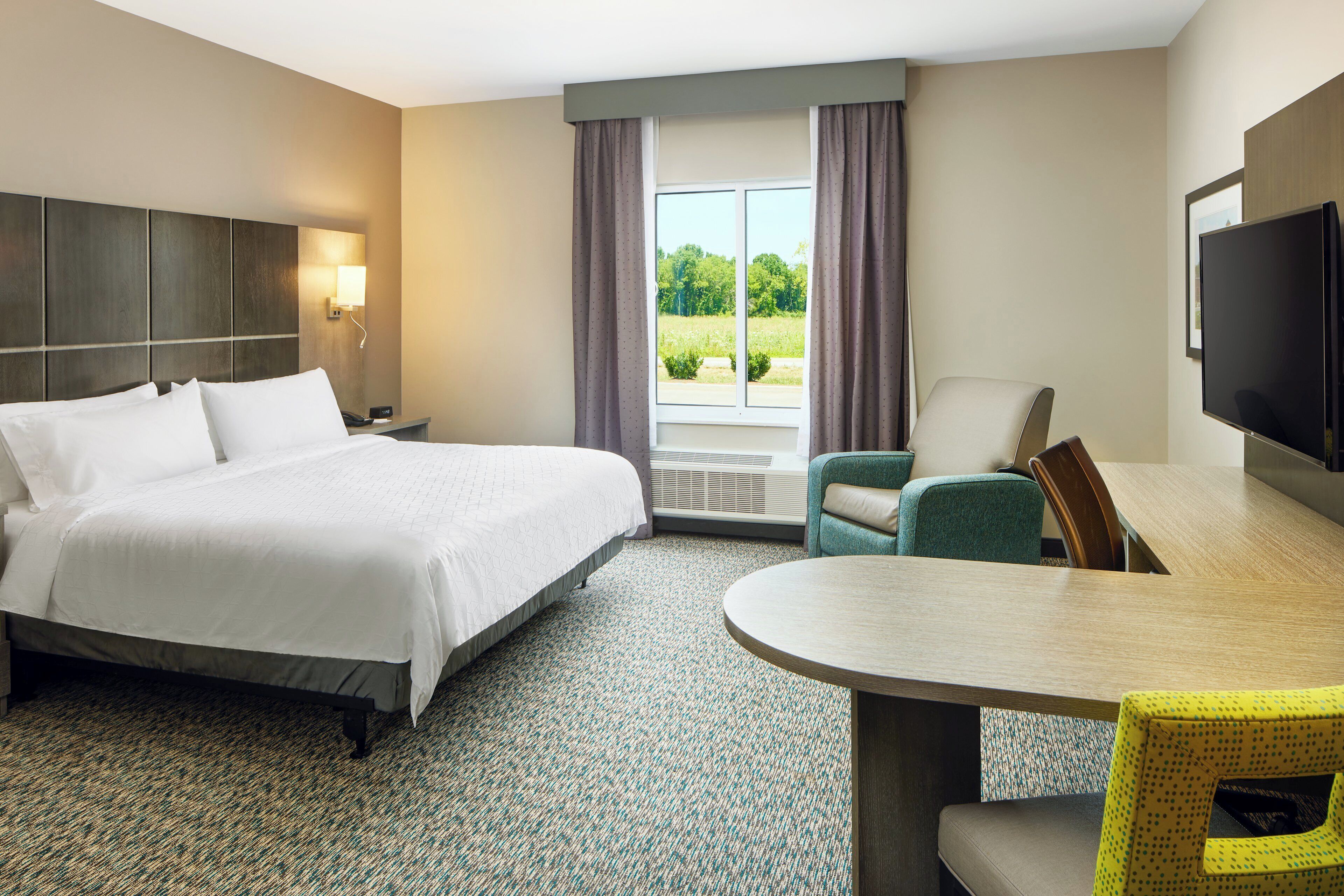 Une chambre d’hôtel avec un grand lit, une table à manger, une télévision et une fenêtre avec des rideaux.