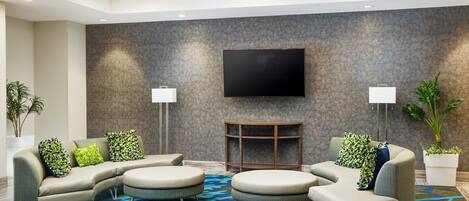 A modern living room with a sectional sofa, round ottomans, a flat-screen TV, and two floor lamps.