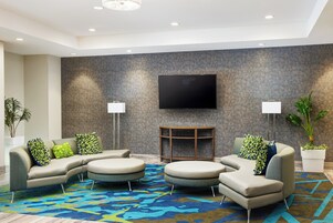A modern living room with a sectional sofa, round ottomans, a flat-screen TV, and two floor lamps.