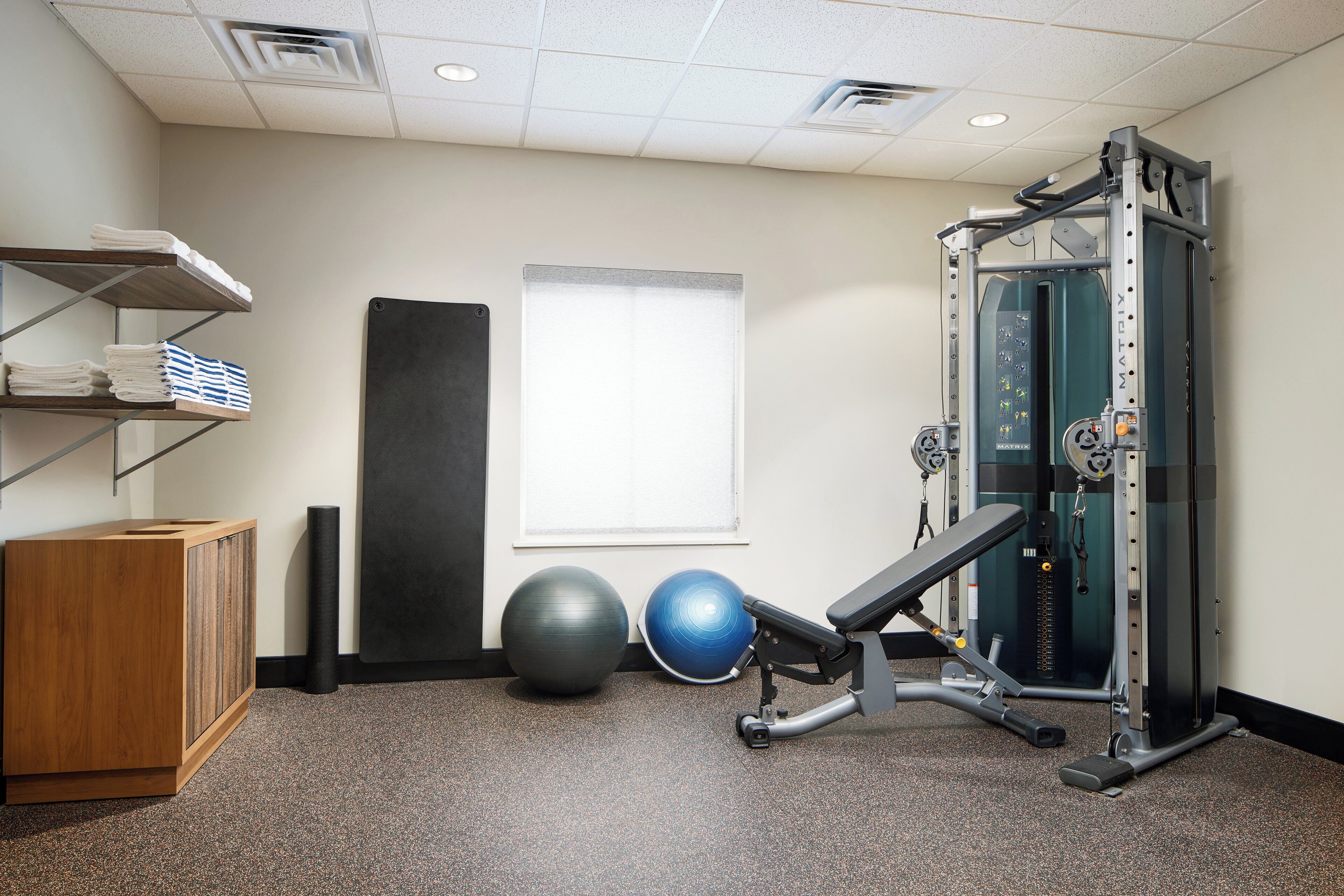 A gym with exercise equipment, a wooden cabinet, and exercise balls.
