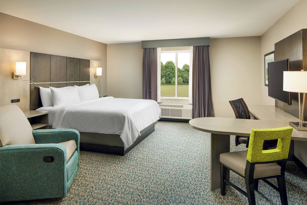 A hotel room with a bed, a desk, a chair, a TV, and a window with curtains.